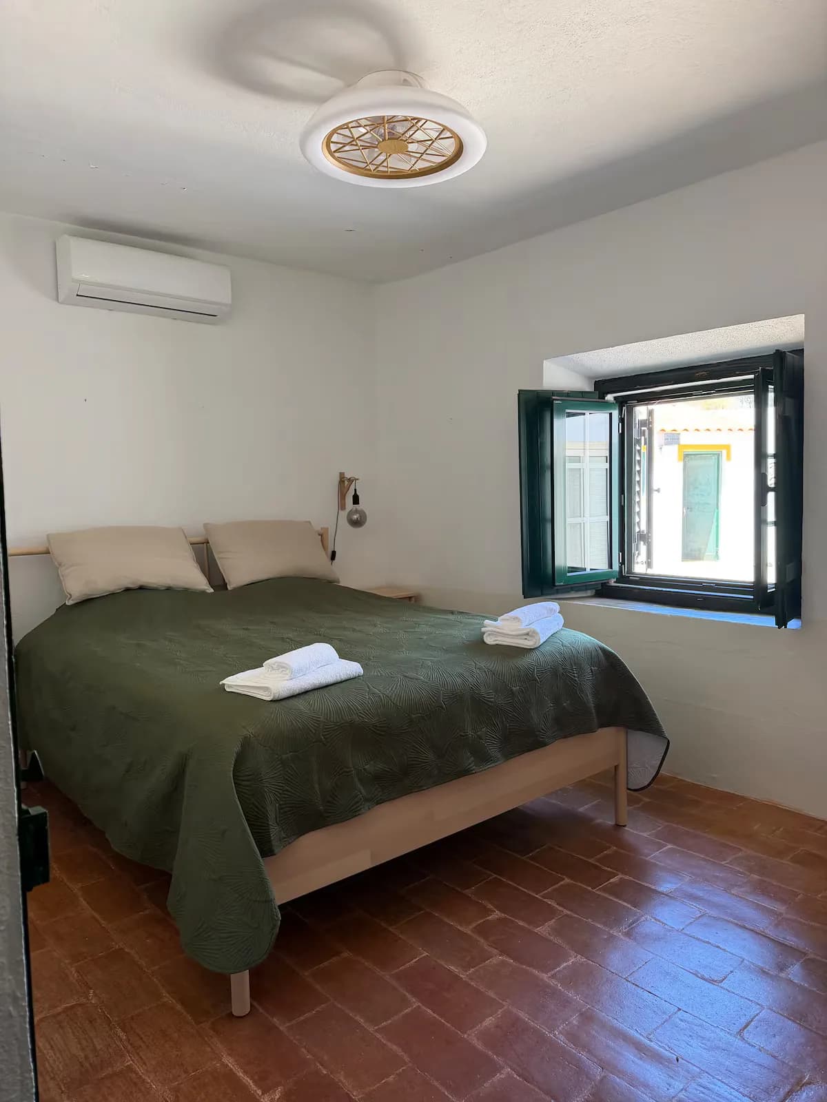 Quarto de casal com colcha verde e ventoinha de teto
