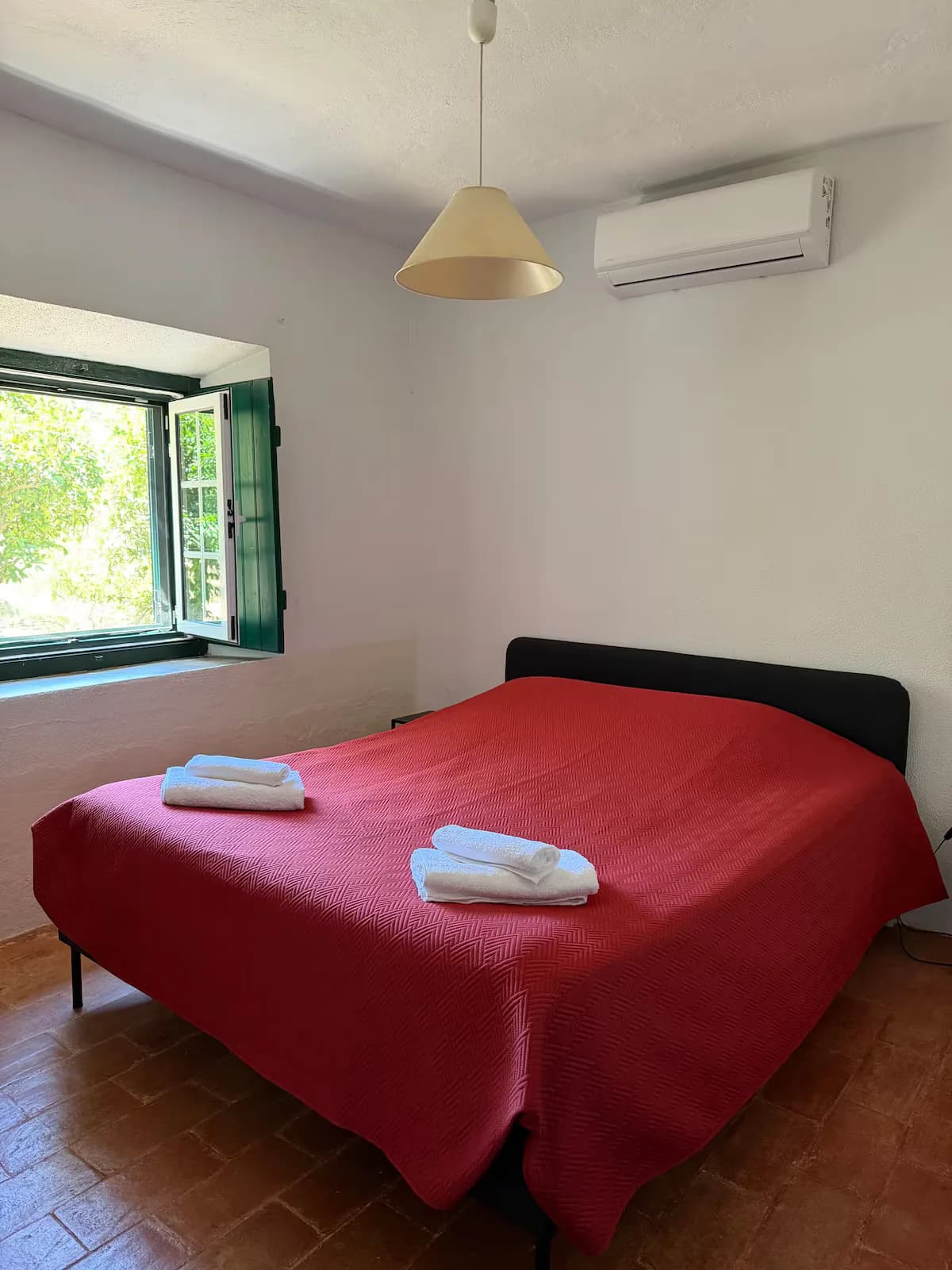 Quarto de casal com colcha vermelha e janela para o jardim